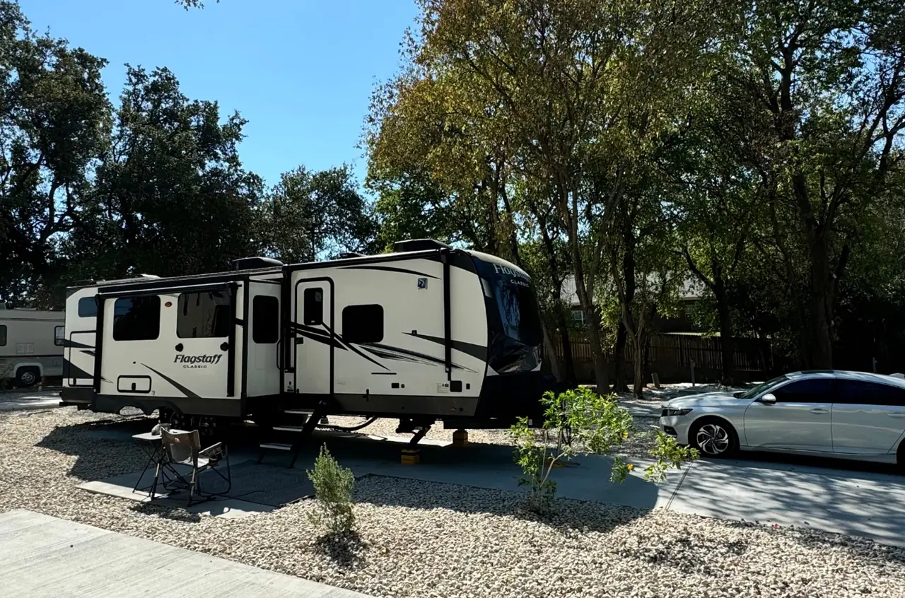 A travel trailer parked beneath oak trees at Oak Hills RV Park
